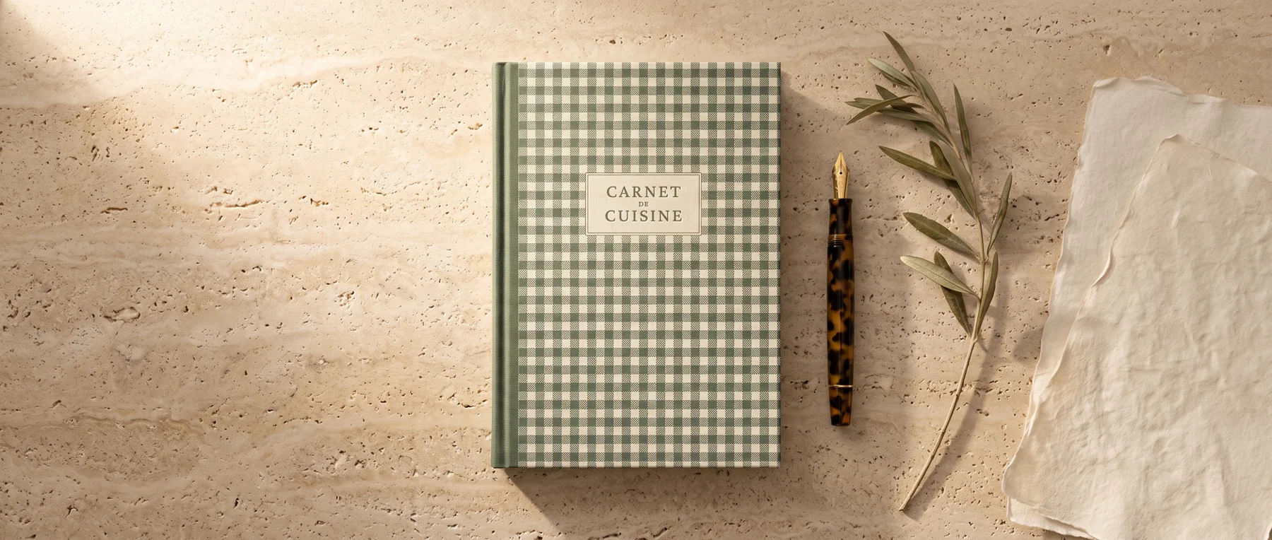 Carnet Vichy sauge sur une table en pierre, accompagné d’un crayon et d’un rameau